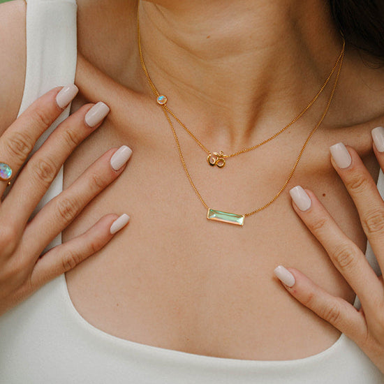 Woman wearing gold bar necklace and om necklace and earrings outdoors