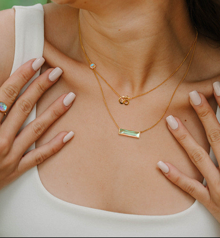 Woman wearing gold bar necklace and om necklace and earrings outdoors