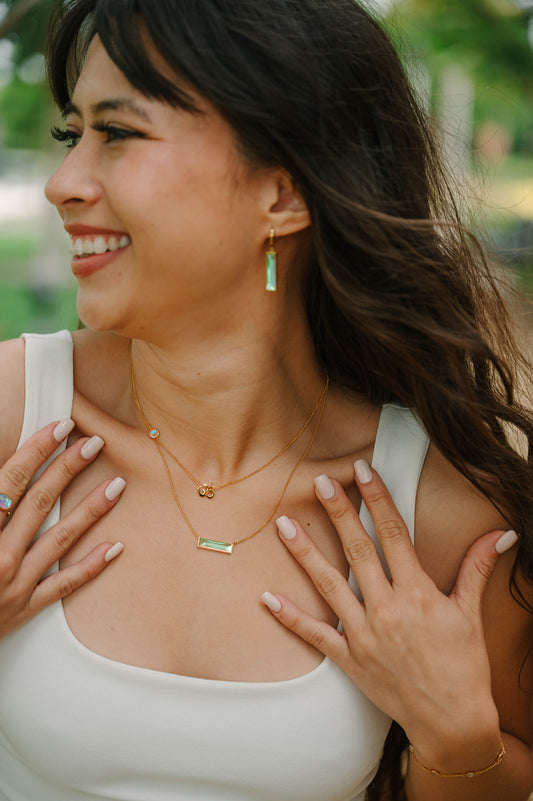 Woman wearing gold bar necklace and om necklace and earrings outdoors