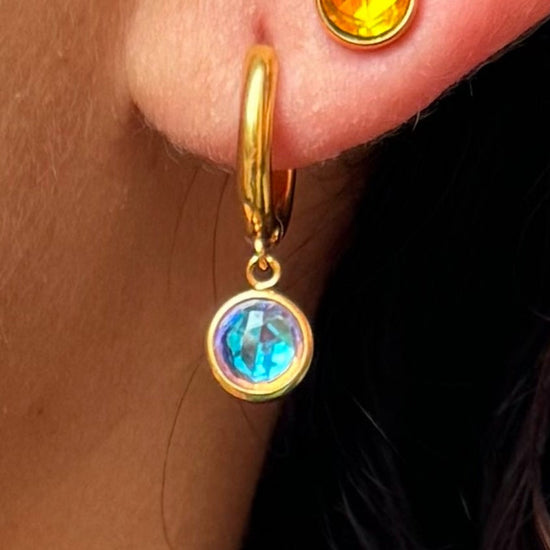 Close-up of a person wearing gold hoop earrings with gemstone drops.