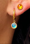 Close-up of a person wearing gold hoop earrings with gemstone drops.