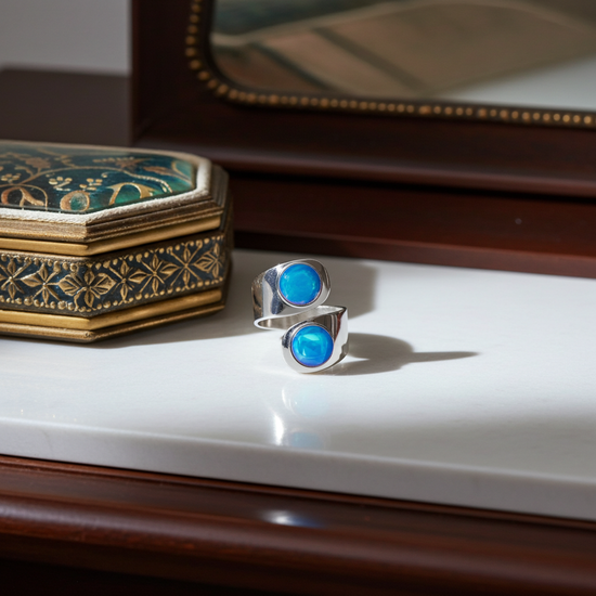 Silver ring with blue gemstone on a white surface next to an ornate box.