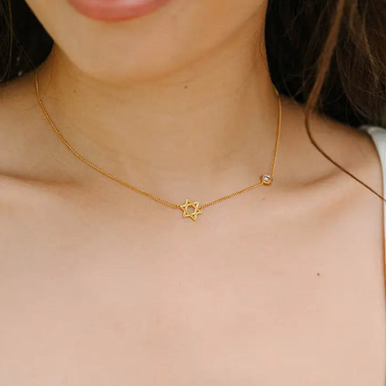 Woman wearing a gold necklace with a star of david shaped pendant.