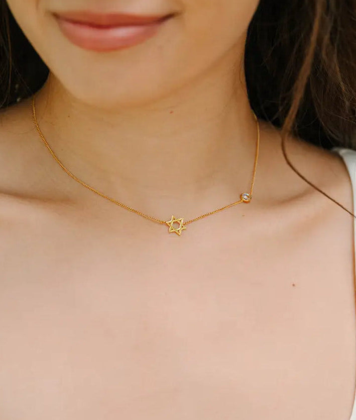 Woman wearing a gold necklace with a star of david shaped pendant.