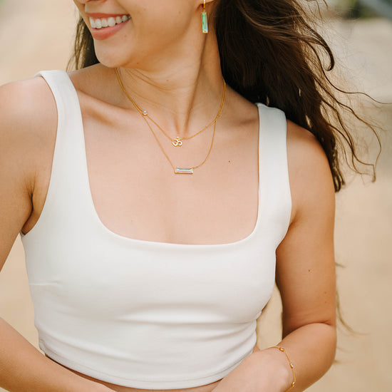 Woman wearing bar earrings a white tank top and gold jewelry outdoors