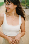 Woman wearing bar earrings a white tank top and gold jewelry outdoors