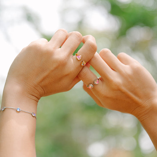 Two hands wearing heart rings  holding each other with blurred greenery in the background