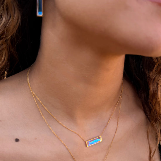 Close-up of a woman wearing gold necklaces and earrings with colorful stones.