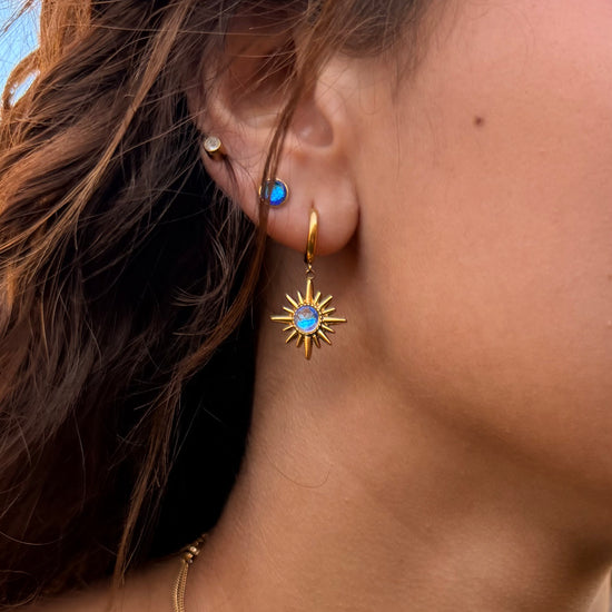 Close-up of a person wearing gold earrings with blue gemstones.