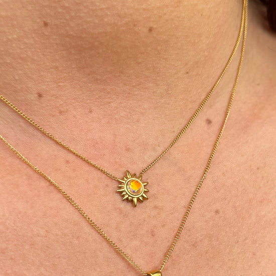 Close-up of a person wearing two gold necklaces, one sun and the other drop on a skin background