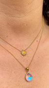 Close-up of a person wearing two gold necklaces, one sun and the other drop on a skin background