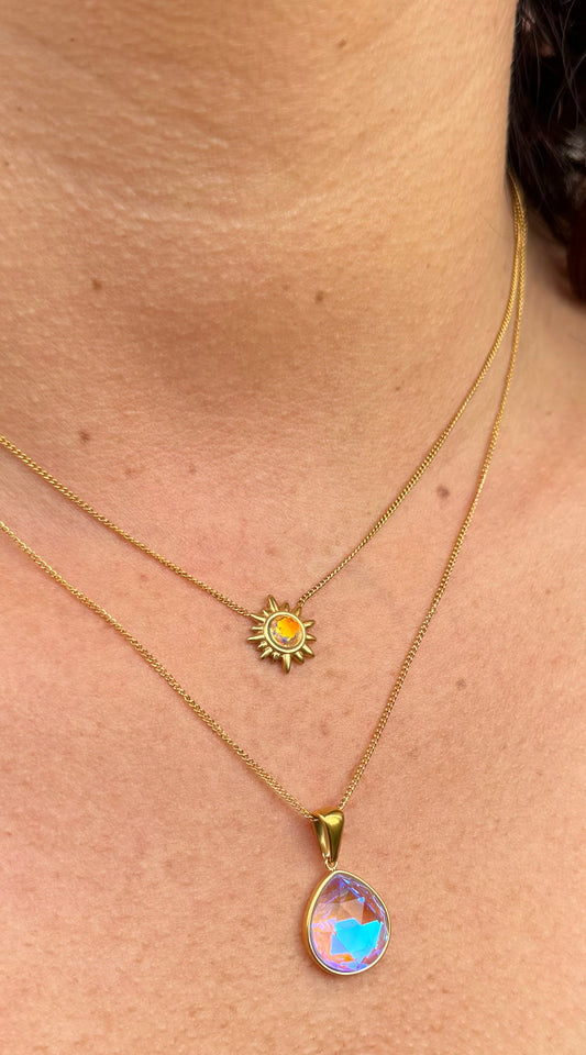 Close-up of a person wearing two gold necklaces, one sun and the other drop on a skin background