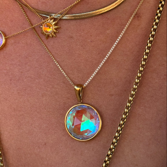 Close-up of a person wearing multiple gold necklaces with colorful pendants on a skin background.