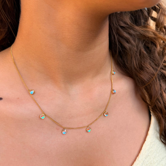 Necklace with small colorful pendants on a person wearing a light-colored top.