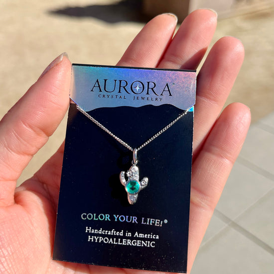 Silver cactus-shaped necklace with green gemstone on an Aurora Crystal Jewelry card.