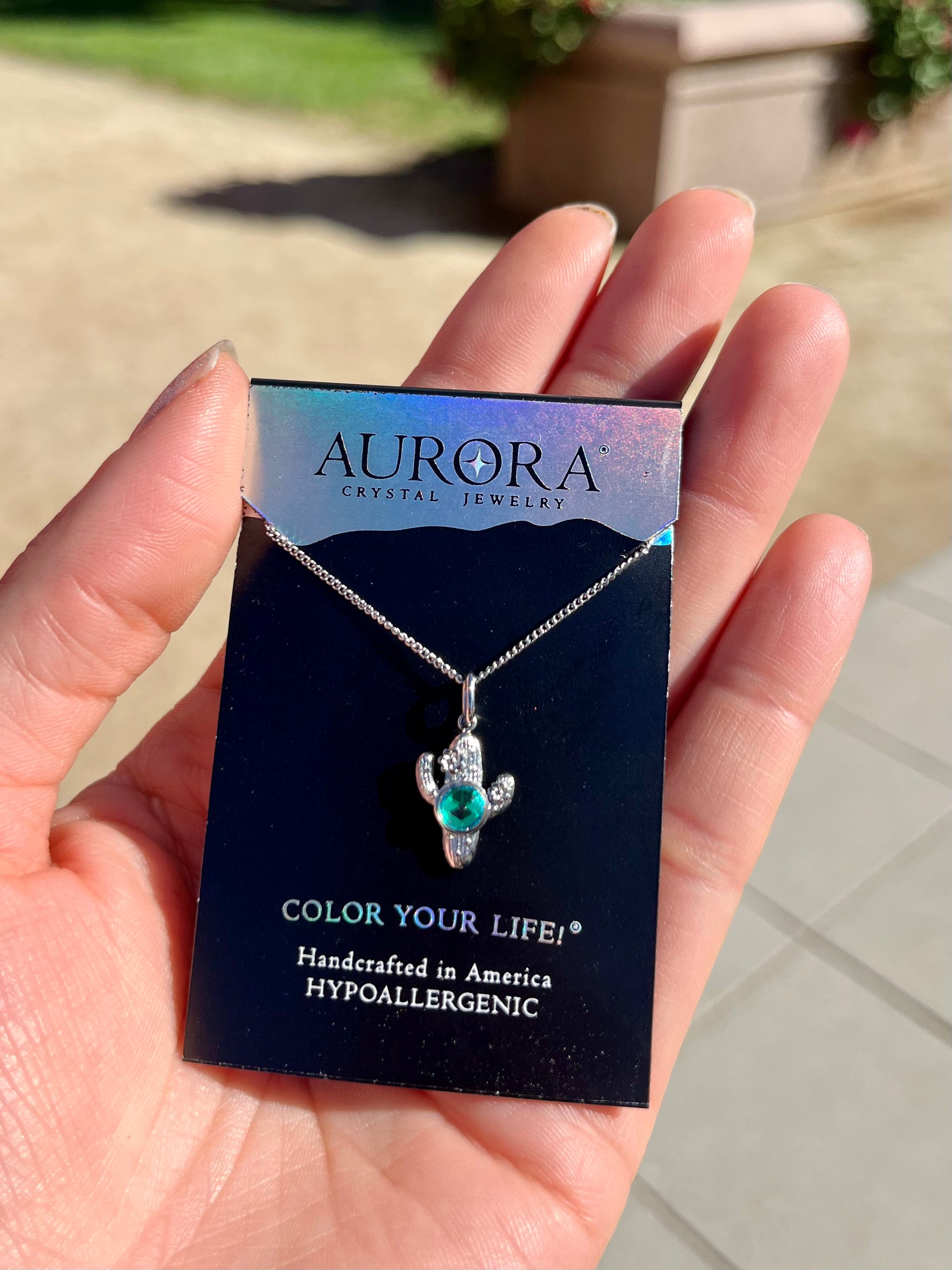 Silver cactus-shaped necklace with green gemstone on an Aurora Crystal Jewelry card.