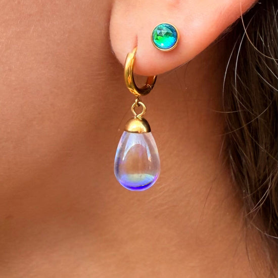 Close-up of an ear wearing a gold earring with a blue teardrop pendant.