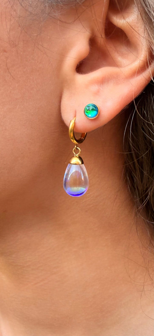 Close-up of an ear wearing a gold earring with a blue teardrop pendant.
