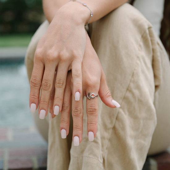 Person sitting outdoors with hands clasped, wearing a sun ring.