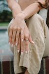 Person sitting outdoors with hands clasped, wearing a sun ring.