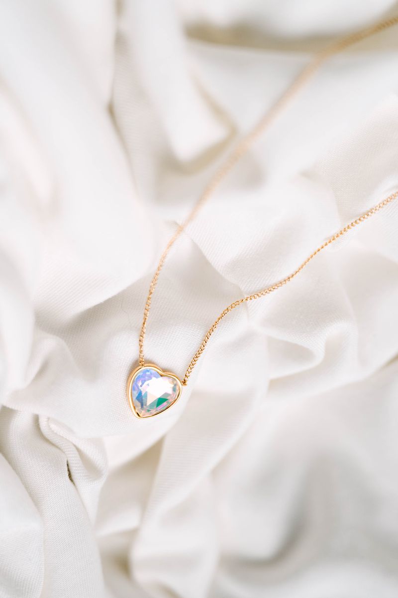 Heart Crystal Necklace, a stunning symbol of love and elegance. This beautiful necklace features a radiant heart-shaped crystal, surrounded by a delicate halo of smaller crystals that enhance its brilliance. Designed to capture and reflect light, this necklace creates a sparkling effect that adds a touch of glamour to any outfit.