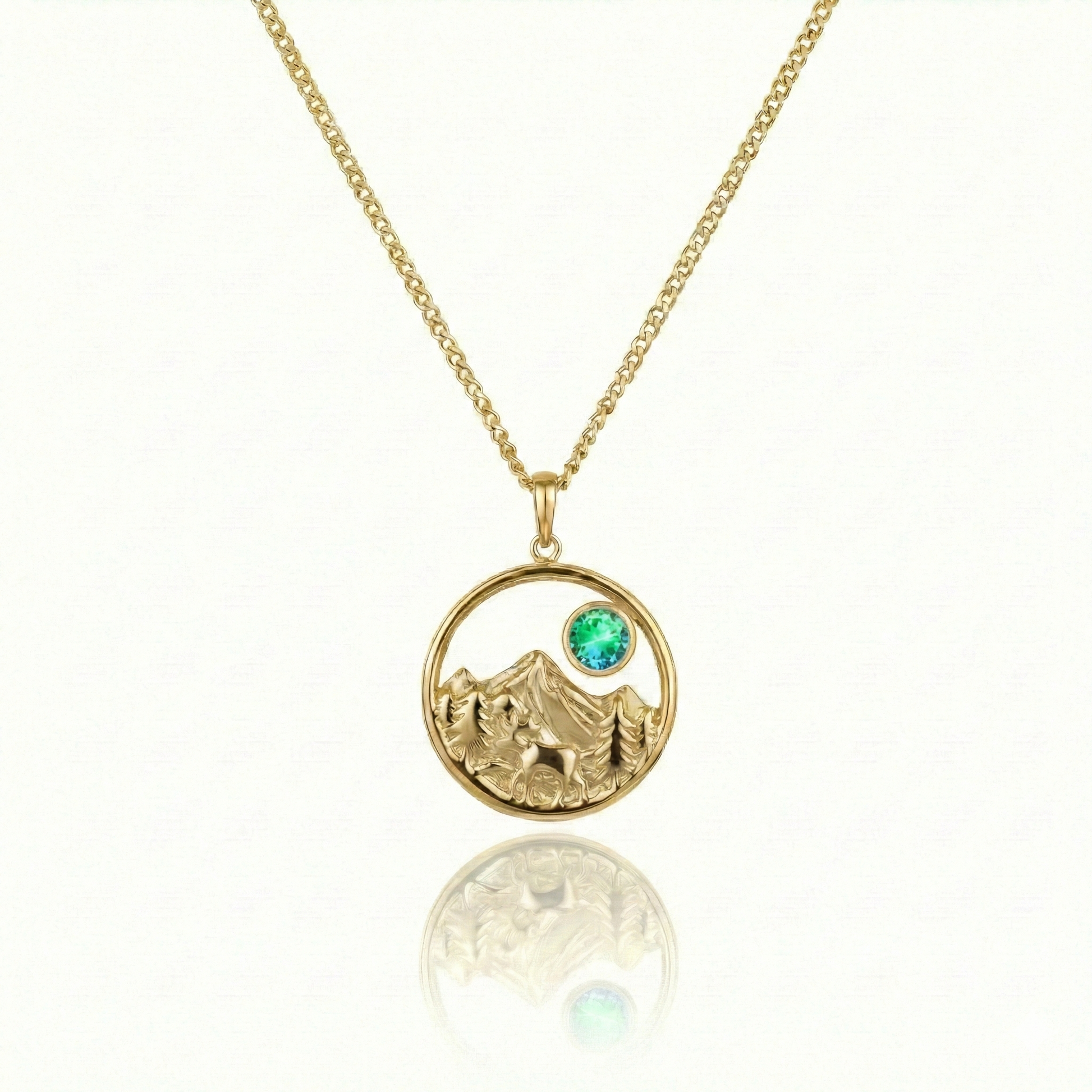 Gold necklace with a moose walking in medow, mountain, and green gem pendant.