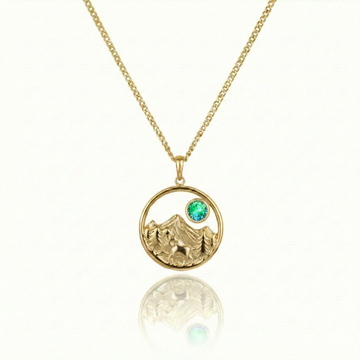 Gold necklace with a moose walking in medow, mountain, and green gem pendant.