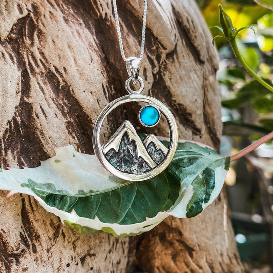 Mountain Pendant featuring a beautiful depiction of mountains under the moon or sun, this pendant captures the serene beauty of nature. The frosted blue pendant includes an 18" sterling silver .7mm box chain.