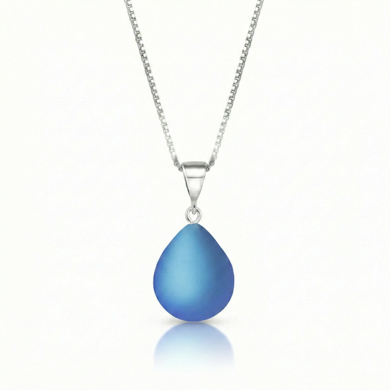 Our best selling crystal X-Small Drop Pendant is a beautiful, easy simple addition to any outfit. Handmade pendants come in a wide variety of colors and shine with an iridescent glow of color from within. Sterling silver .7mm box chain, 18" included with the frosted blue pendant.